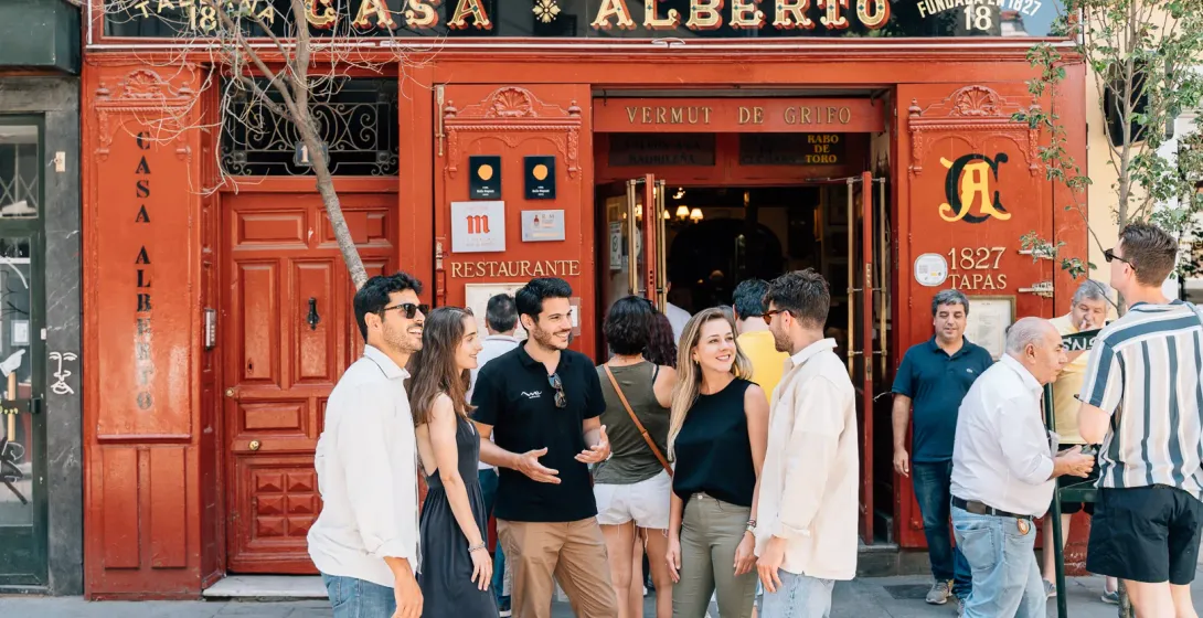 A tour guide talks to tourists in front of the red facade of the historic Casa Alberto tavern in Madrid.