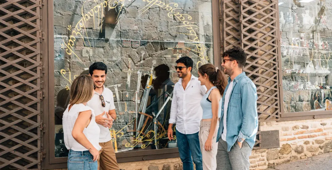 A group of five young adults talking in front of a shop with gold script on its display window.