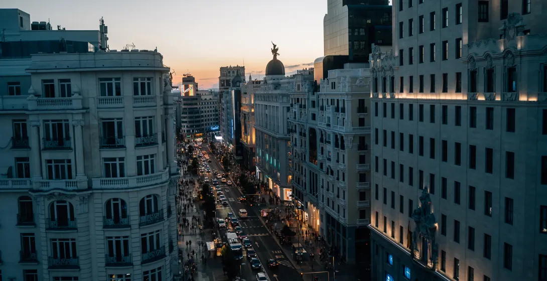 An elevated view of Madrid's busy Gran Vía street at sunset, bustling with cars and pedestrians on the sidewalks.