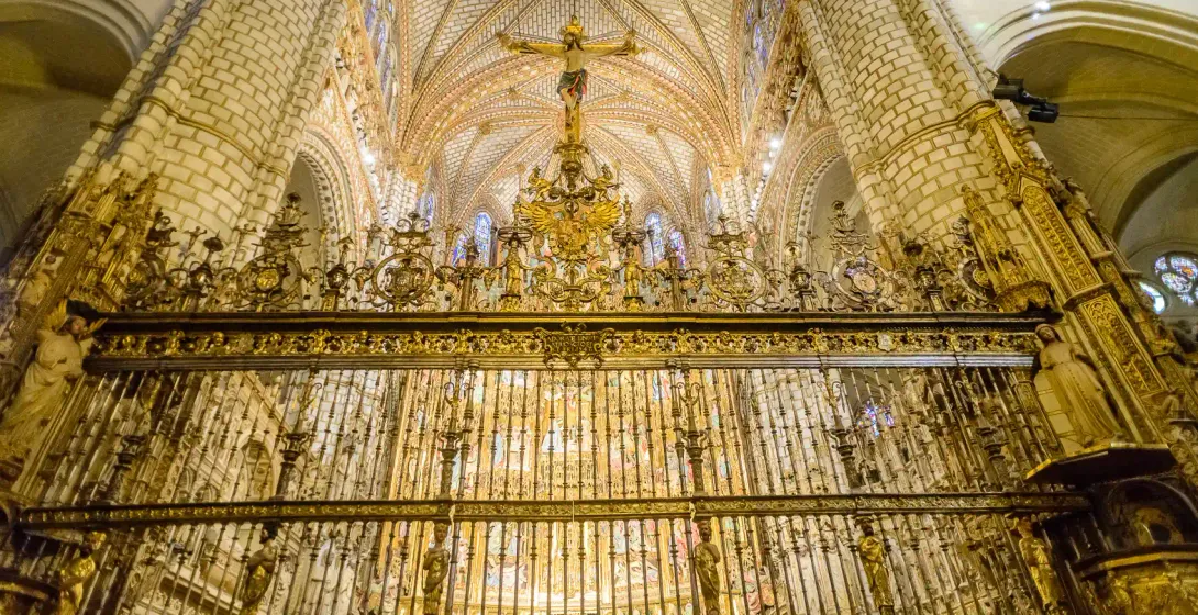 Ornate golden chancel screen below a crucifix and high vaulted ceiling inside the Toledo Cathedral, Spain.