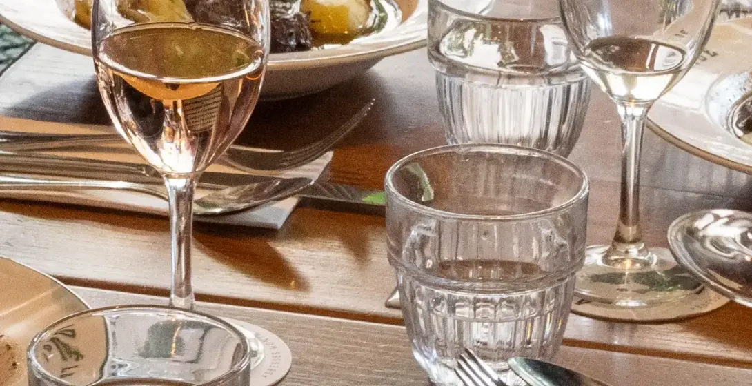 A dining table set with plates of stew, one reading 'ADÉLAÏDE', glasses of water and rosé wine, and a bread basket.