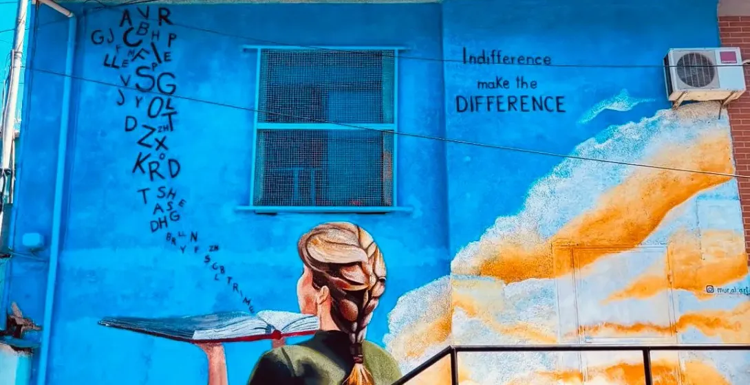 Colorful street art mural of a woman holding a book on a blue building.