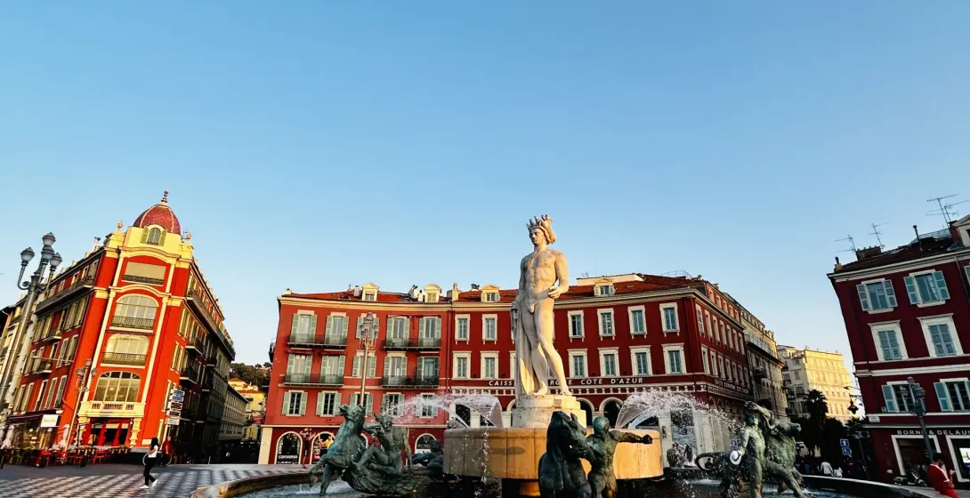 Fontaine du Soleil (Sun Fountain) in Nice, with the statue of Apollo and bronze figures, surrounded by red buildings under...
