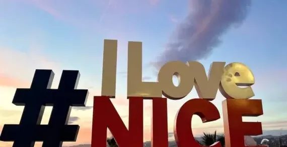 Large '#ILoveNICE' sign illuminated at dusk, with a soft pink and blue sky over the city and sea in Nice.