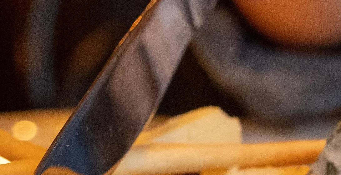 Close-up of a hand with red nail polish cutting a slice of white-rinded cheese on a plate with breadsticks.
