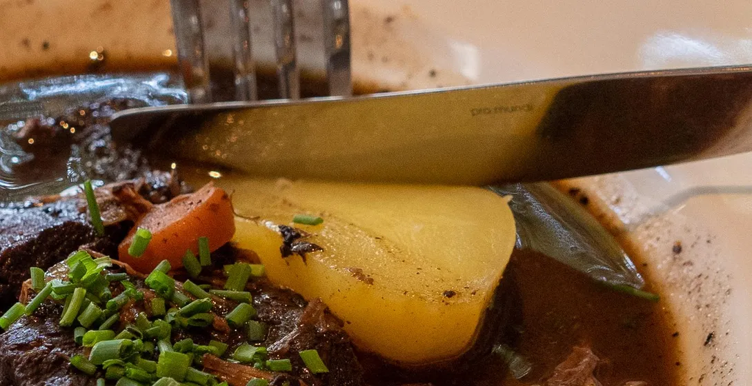 Close-up of a French stew with potato and fresh chives, a fork and knife cutting into it.