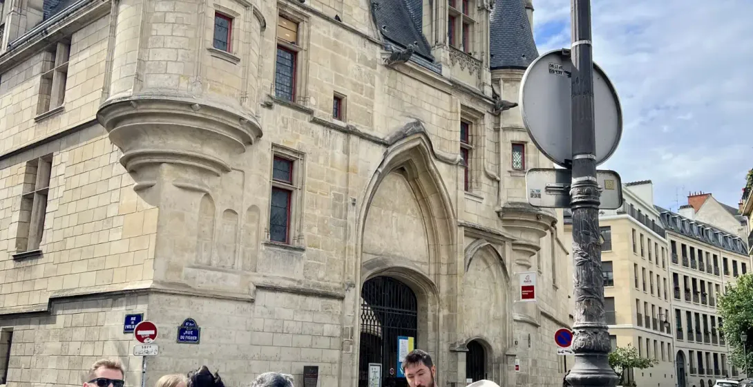 Tour guide addressing a small group of tourists in front of the historic Hôtel de Sens building in Paris on a cloudy day.