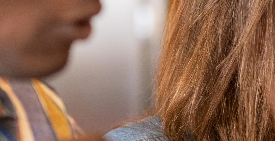 Close-up of two people in profile, one with dark skin and striped shirt, the other with brown hair and denim shirt, conver...