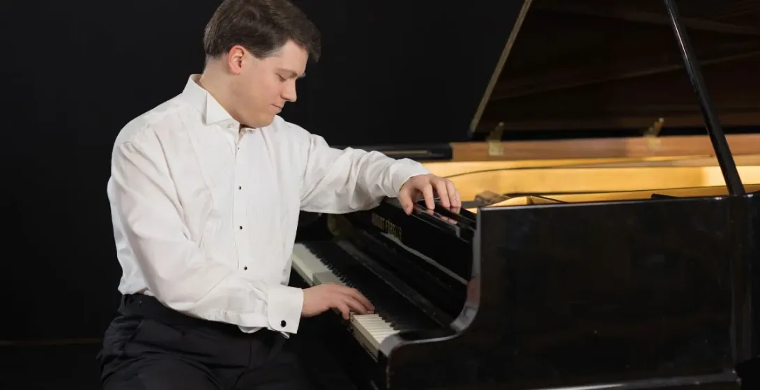 A pianist plays a grand piano in a dark setting.