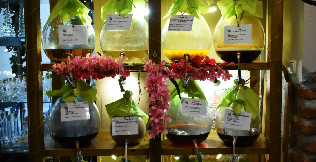 Glass dispensers filled with traditional Polish nalewka liqueurs on wooden shelves in a Krakow shop.