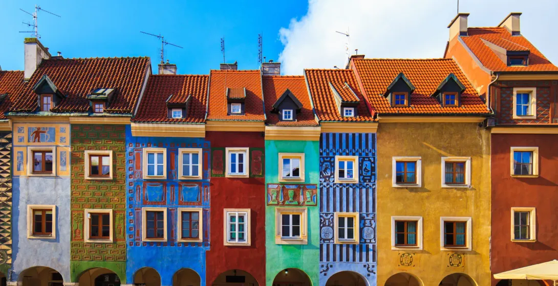 Row of colorful historic houses with tiled roofs and arched ground floors on a cobblestone square in Poznan.