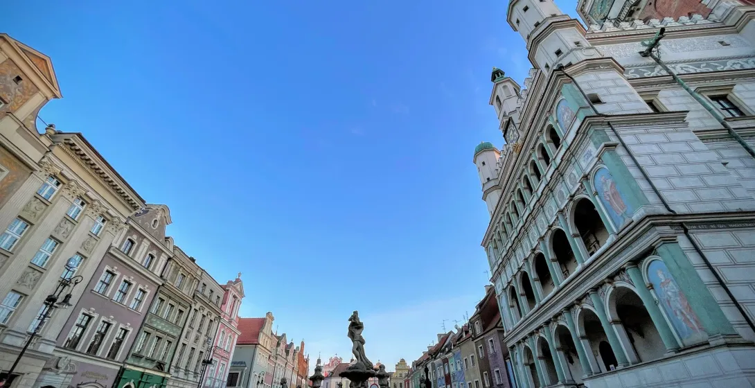 Panoramic view of Poznań Old Market Square with colorful tenement houses, a large fountain, and the ornate Renaissance Tow...