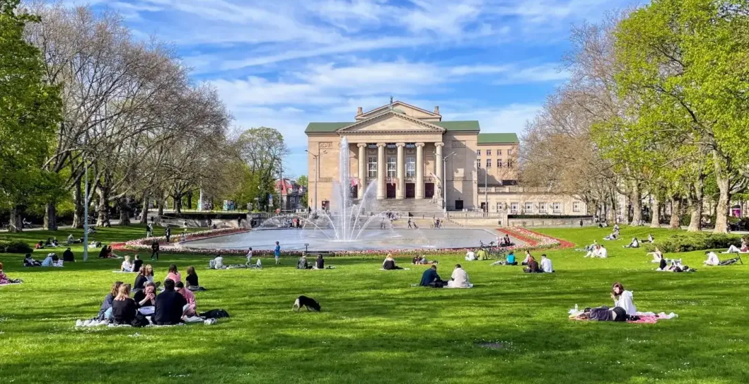 Gebäude des Großen Theaters, Springbrunnen und Menschen entspannen auf grünem Gras im Park in Posen an einem sonnigen Tag.