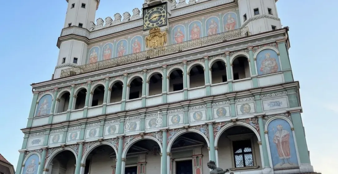 Renaissance Town Hall in Poznan with ornate facade, arcades, frescoes, clocks, and green spires under a blue sky, fountain...