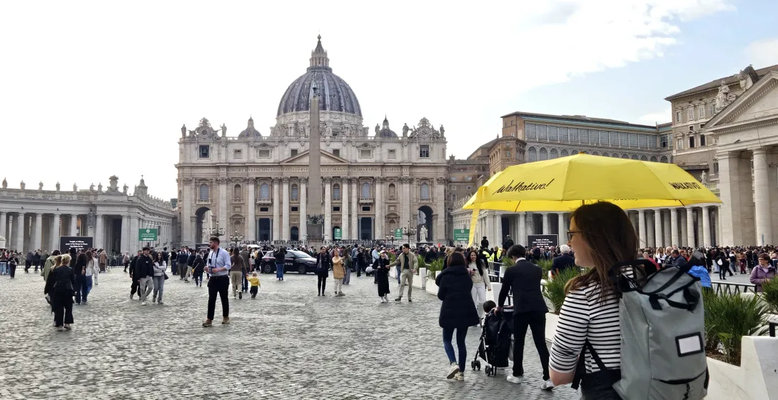 Crowded St. Peter's Square with St. Peter's Basilica, an obelisk, and colonnades under a partly cloudy sky. A yellow Walka...