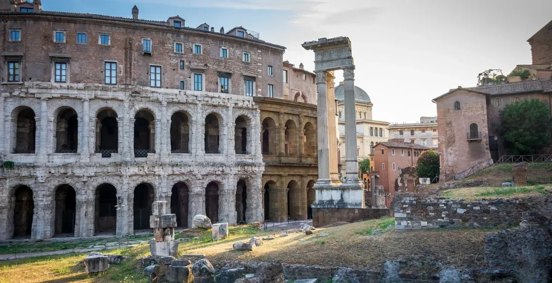 Ancient Theatre of Marcellus ruins with arched facade, modern buildings above, and Roman columns and debris in foreground.