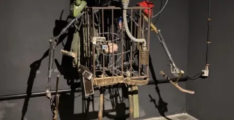 A captivating metal sculpture resembling a caged robot, displayed in a dark gallery.
