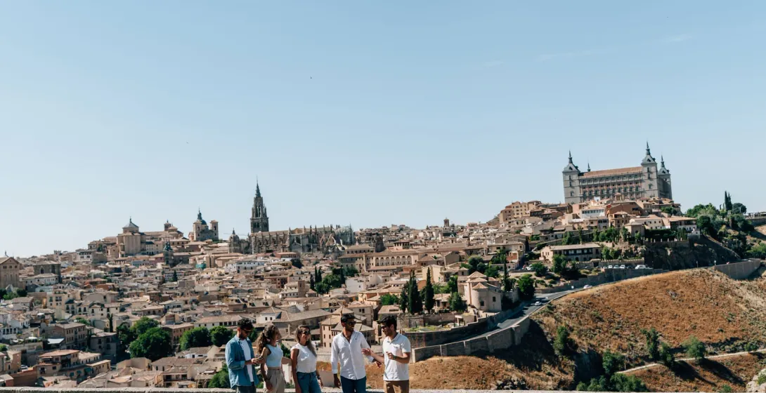 A group of people at a viewpoint overlooking the historic city of Toledo, Spain, on a sunny day.