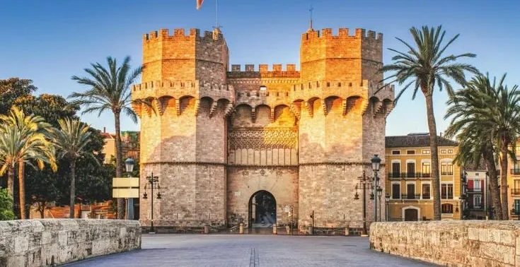 The Serranos Towers, a historic city gate in Valencia, viewed from a bridge at sunrise.