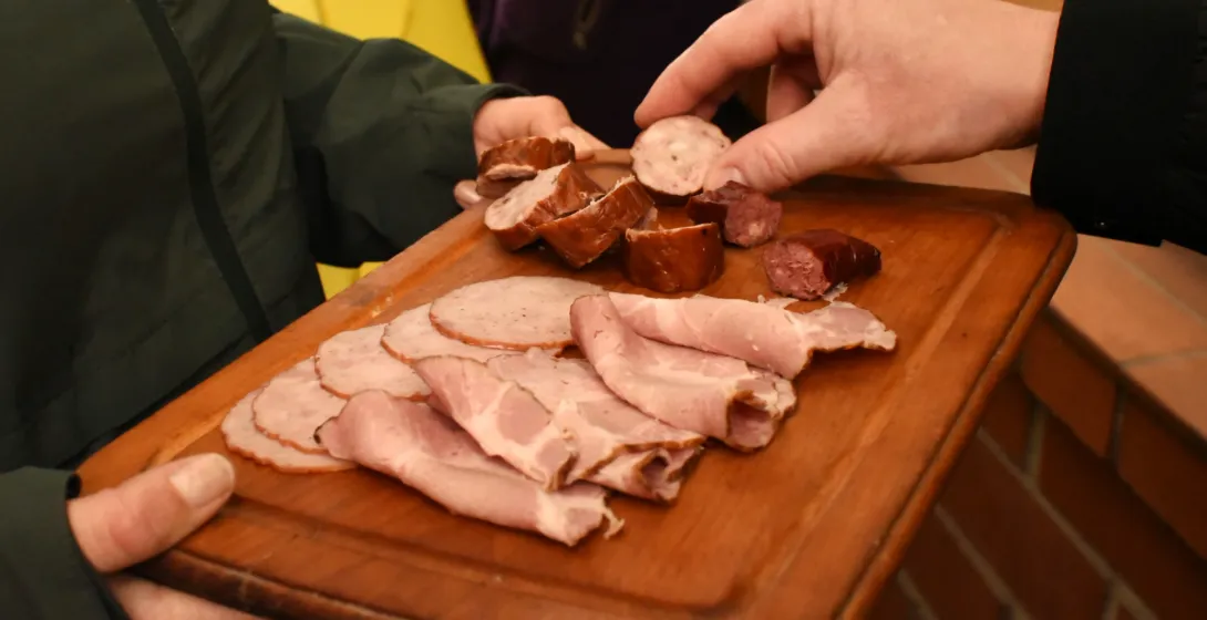 Two people sharing a wooden board with traditional sliced meats and sausage tasting portions.