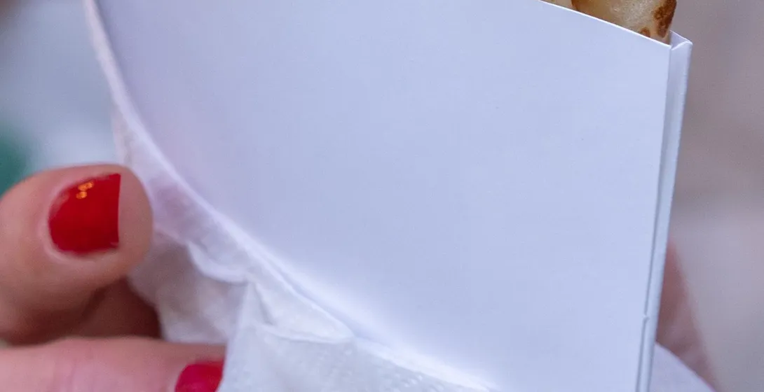 Close-up of a person's hand with red nail polish holding a folded crepe in a white paper holder.