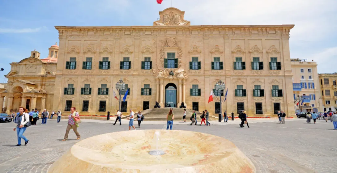 The Auberge de Castille, an ornate Baroque building with green shutters and the Maltese flag, stands on Castille Square wi...