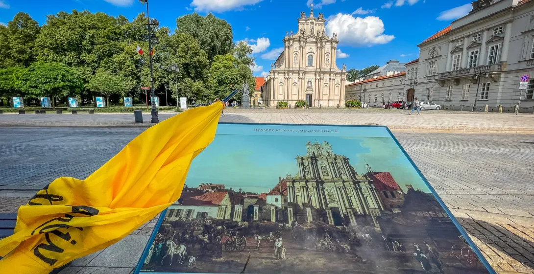 The Church of the Visitandines in Warsaw, a light-colored baroque building, seen behind a historical information board.
