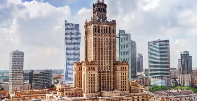 Palace of Culture and Science in Warsaw, a tall building with a clock tower, surrounded by several modern glass skyscraper...