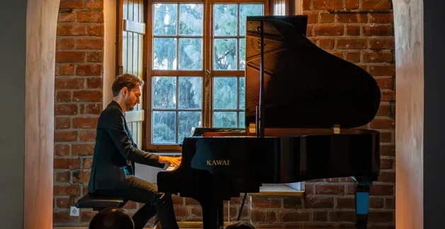 Pianist playing a grand piano during an intimate concert in a brick room with arched doorways in Warsaw.