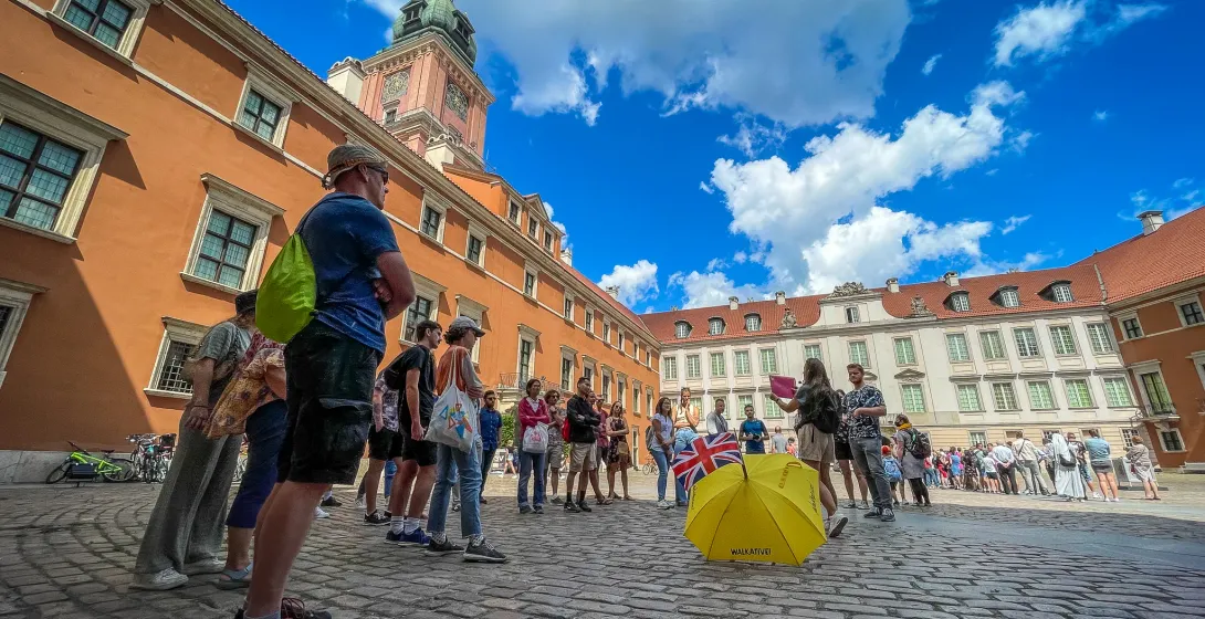 Tour group with guide and yellow umbrella on a cobblestone courtyard in front of Warsaw Royal Castle.