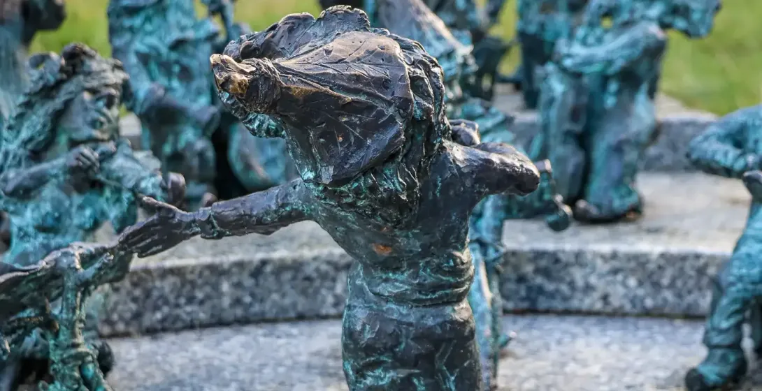 Group of bronze dwarf sculptures with green patina in Wroclaw. One dwarf in foreground extends its arm towards another on ...