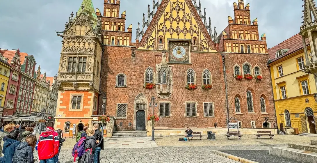 Wroclaw Old Town Hall, a large brick gothic building with a tall clock tower, stands on a cobblestone market square with a...