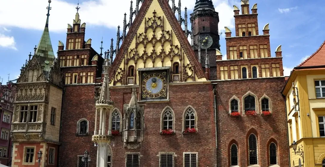 Gothic brick Old Town Hall in Wroclaw with a large clock, ornate gables, and a tall spire. People are gathered in the cobb...