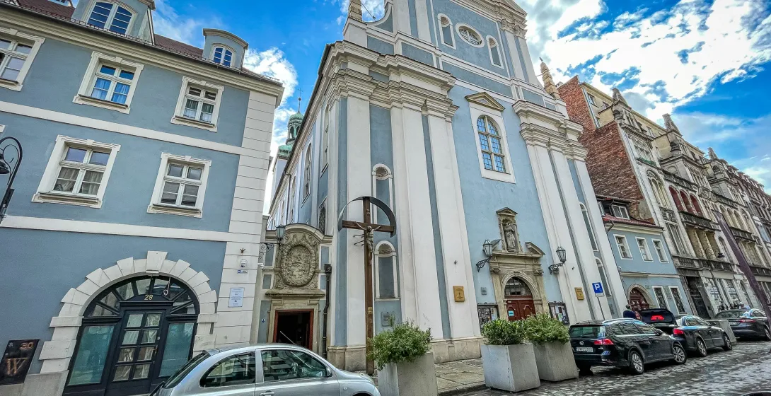 The light blue baroque facade of St. Anthony of Padua Church on a cobblestone street in Wrocław under a blue sky.