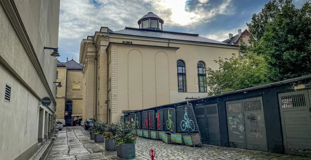 Cobblestone alleyway leading to the White Stork Synagogue in Wroclaw under a cloudy sky. Potted plants and bicycle racks a...