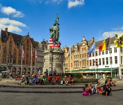 Tourists enjoying the Market Square in Bruges, Belgium, with the Jan van Eyck statue in the background.
