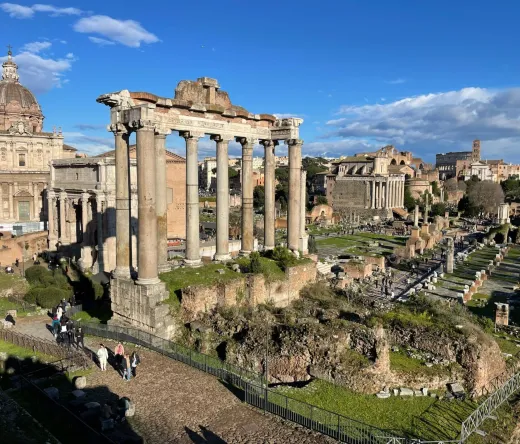 Panoramic view of the Roman Forum in Rome, Italy, with tourists exploring the ancient ruins.