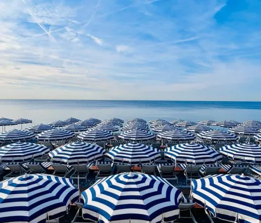 Rows of blue and white striped beach umbrellas and chairs on a Nice beach.