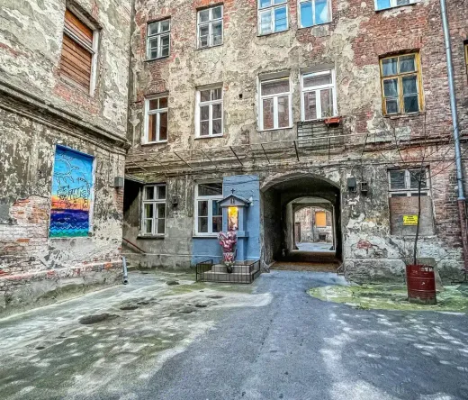 Explore a hidden Warsaw courtyard with aged brick buildings, street art, and a small shrine.