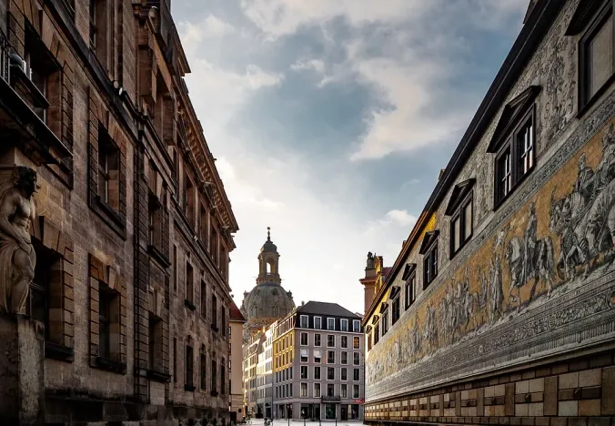 Cobblestone street in Dresden, Germany, with historic buildings and a fresco.