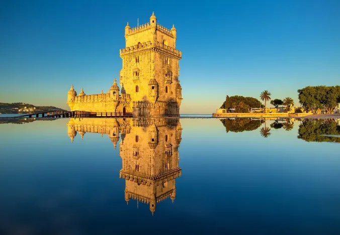 Belém Tower in Lisbon, Portugal, reflected in the water at sunrise.