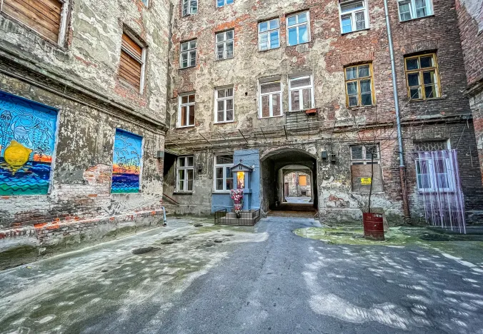 Explore a hidden Warsaw courtyard with aged brick buildings, street art, and a small shrine.