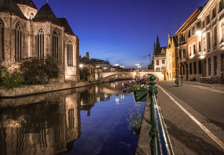 Ghent's charming canal at night, reflecting historic buildings.
