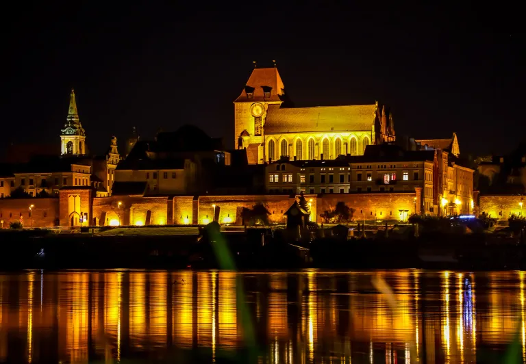 Night view of Toruń's Old Town reflected in the Vistula River.