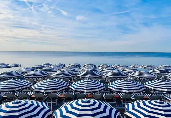 Rows of blue and white striped beach umbrellas and chairs on a Nice beach.