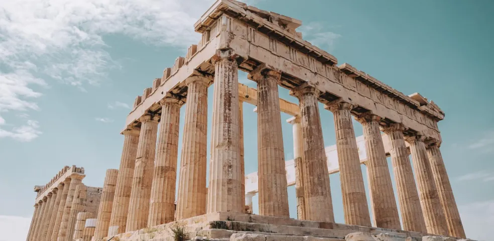 View of the Parthenon temple on the Acropolis in Athens, showing several Doric columns under a partly cloudy sky.