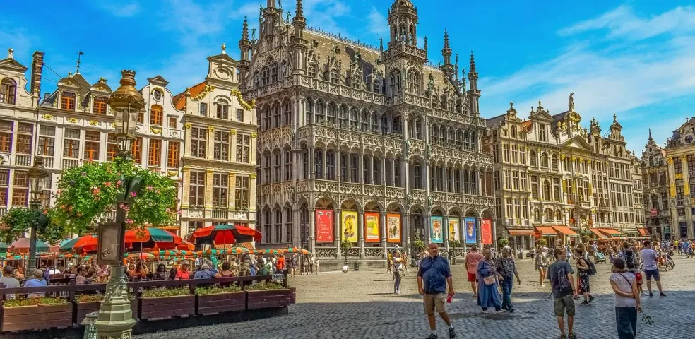 Grand Place in Brussels with ornate historic buildings, outdoor cafes, and people walking on a sunny day.