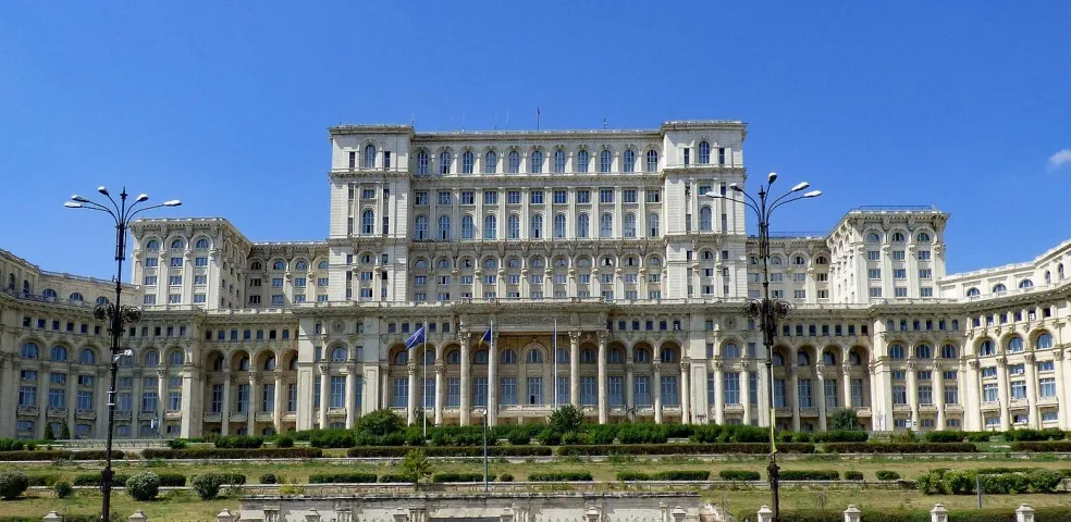 The Palace of the Parliament in Bucharest, a massive white building with many windows and columns, set against a blue sky wit