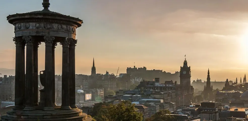 The Dugald Stewart Monument in Edinburgh's Calton Hill at sunrise, overlooking the city skyline with castle and monuments.