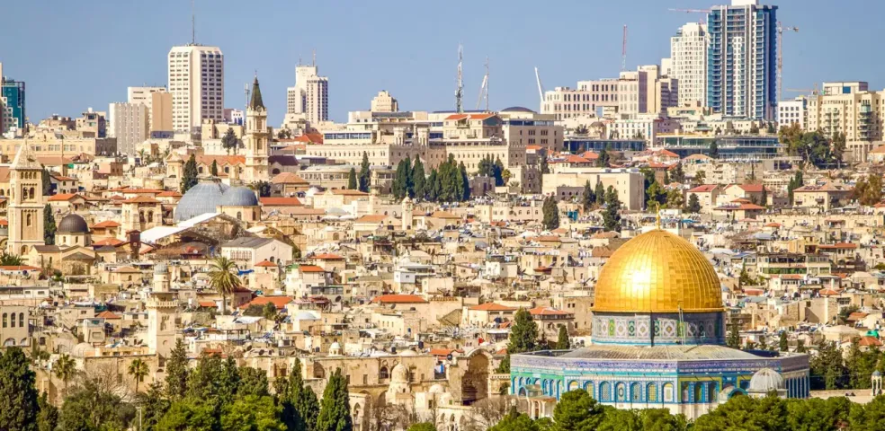 View of Jerusalem with the golden Dome of the Rock in the foreground and the Old City buildings and modern high-rises behind.